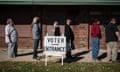 Five people stand in line behind a white sign pointing to the right for voter entrance