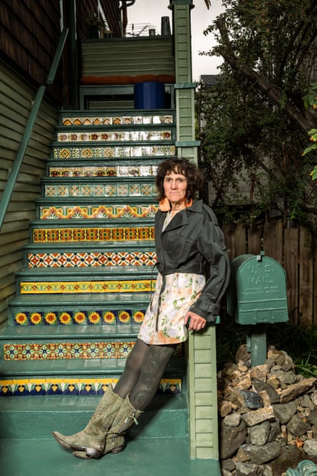 Woman with long earrings standing at base of outside stairway decorated with tiles.