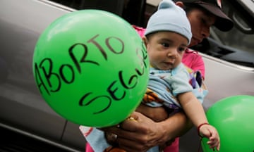 A man carries his son and a balloon reading 'Safe Abortion'