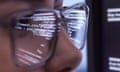 Computer code on a screen is reflected in a woman's glasses