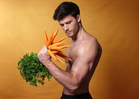 Bodybuilder model holds carrots like a weight, with elbow bent, against orange background