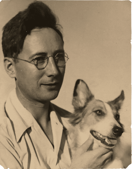 sepia-toned photograph of a man wearing glasses and a white button down, posing with his smiling sheepdog