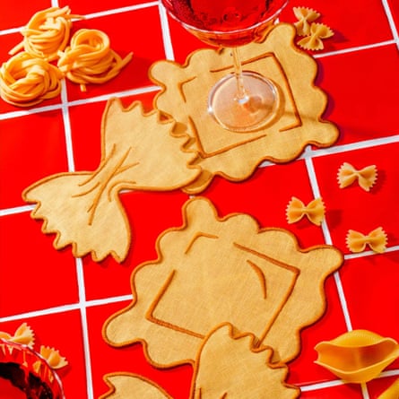 Pasta shaped linen napkins are scattered across a red tiled surface with pasta shells arranged for decoration/