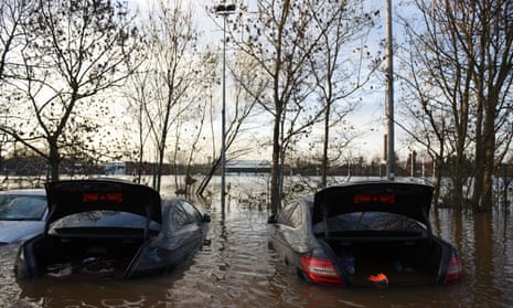 Vehicles stand submerged in flood waters, one with an industrial waste bin on its roof, in the car park of Carlisle United FC in Carlisle.