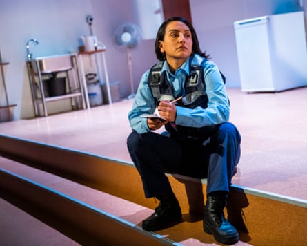 Woman sits on a step in a stage set of a bare kitchen
