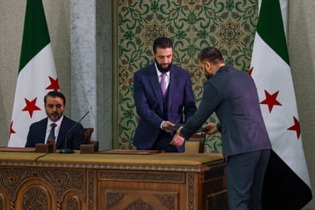 Syria’s interim president, Ahmed al-Sharaa, centre, prepares to sign a temporary constitution in Damascus