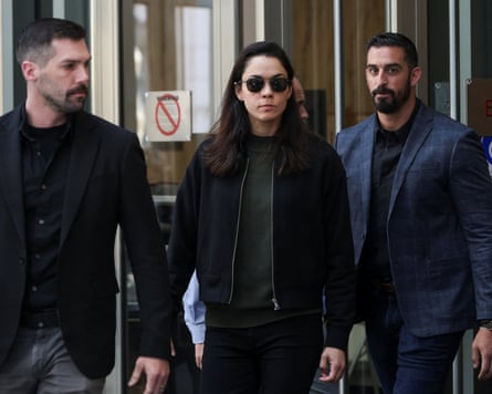 Woman in sunglasses flanked by two men walks into a building.