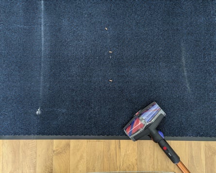 A piece of blue carpet with fragments of cat litter on it and the head of a Dyson vacuum cleaner on the edge