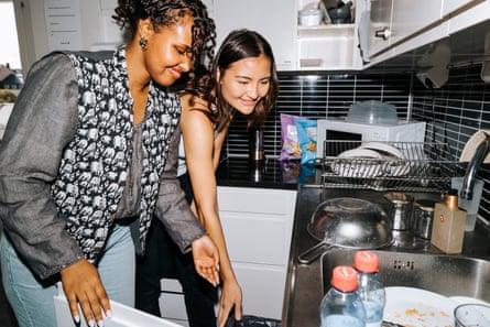 Smiling young woman helping female roommate working in dorm room kitchen