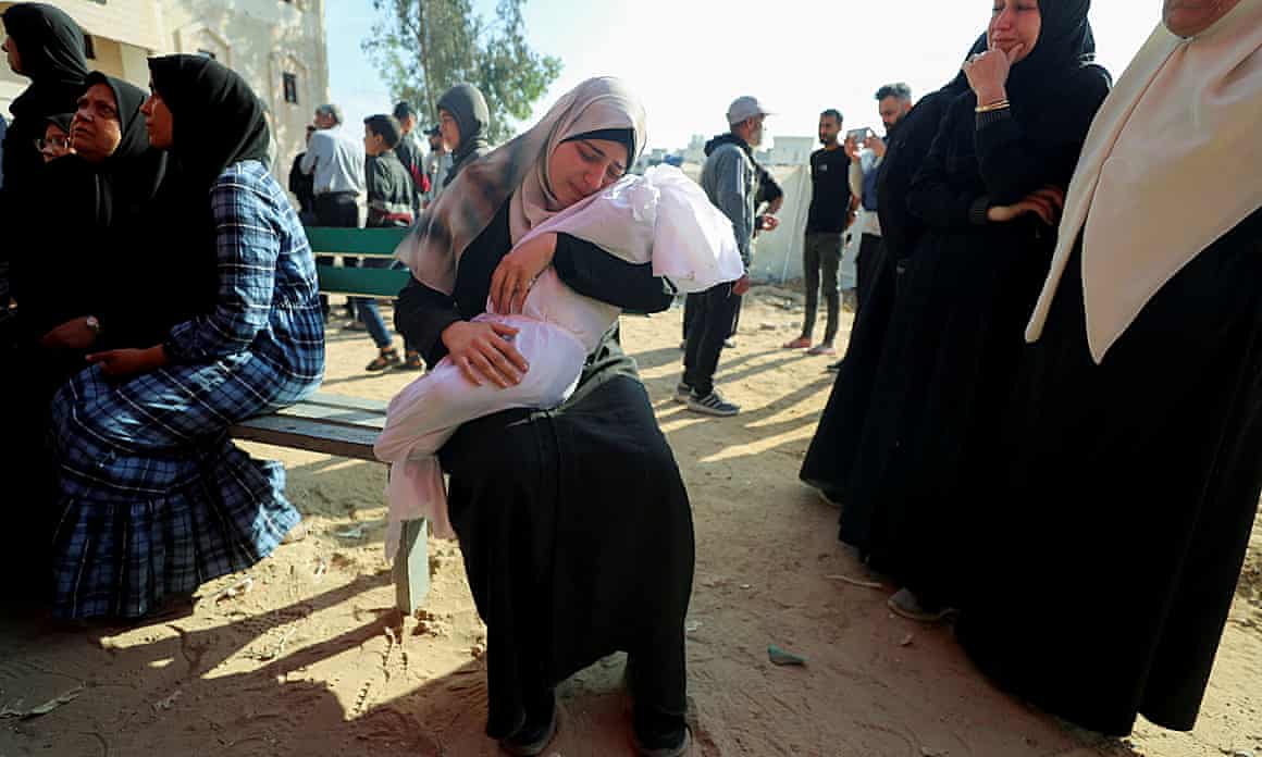 A woman holds the body of a child that is wrapped in a white shroud