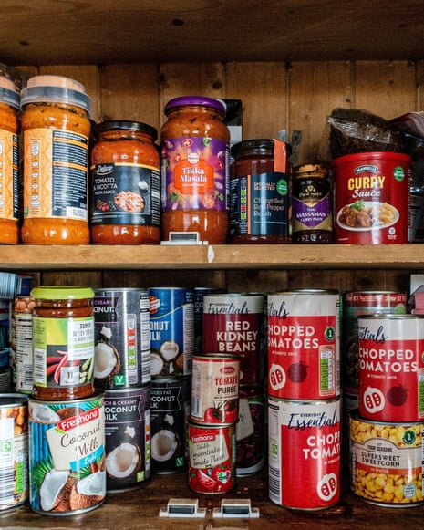 Wooden pantry shelves hold jars of curry sauce and many tinned goods like tomatoes and beans