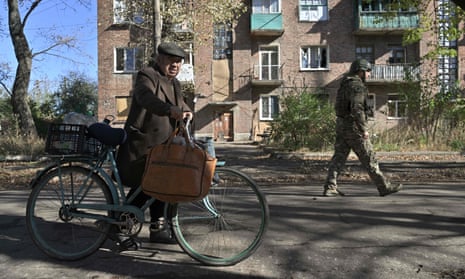 A Ukrainian police officer walks next to 84-year-old Mykola pushing his bicycle in Chasiv Yar