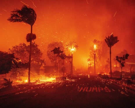 A fire blazes on street lined by palm trees, the sky an orange-red hue