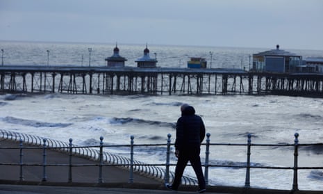 A man walks along the Brighton seafront on a dark and blustery day.