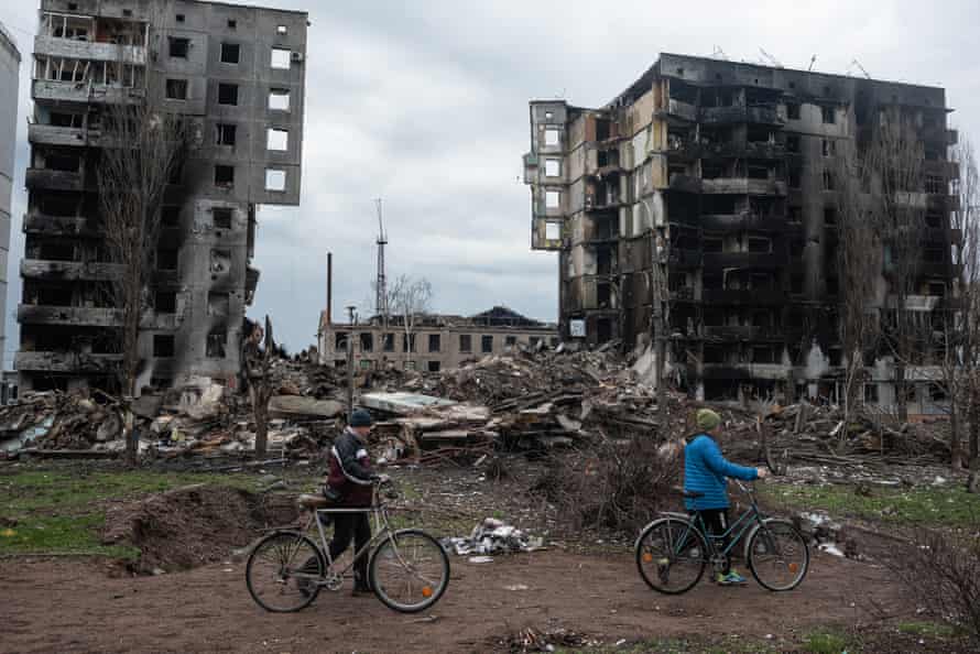 Two cyclists push their bicycles in front of a destroyed apartment building in Borodianka, Ukraine.