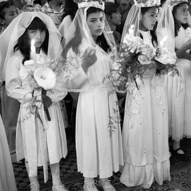 A row of girls carrying flowers and dressed with veils for their first communion