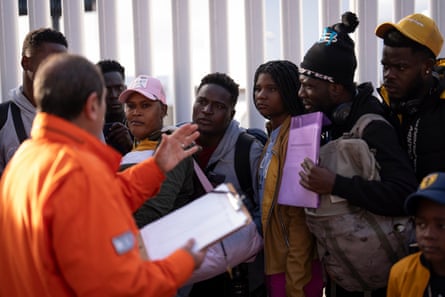 A man in an orange jacket speaks to a group of people