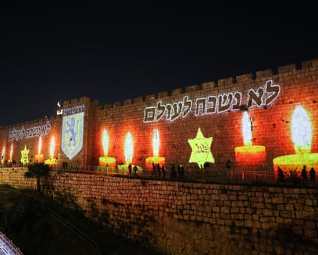 People walk by the Old City walls illuminated with the message ‘We will never forget’ on the eve of Israel’s Holocaust memorial day (Yom HaShoah) in Jerusalem on Monday