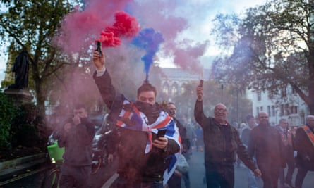 Men holding blue, red and white smoke flares, one looking at his mobile phone.
