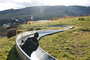 Hesse, Germany. A man rides on a summer toboggan run in the winter sports resort of Willingeny. Due to mild temperatures and a lack of snow, the operator has kept the attraction open