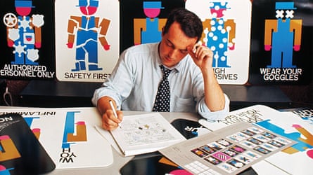 Designer Lance Wyman posting in front of a collection of work-related signage he designed.