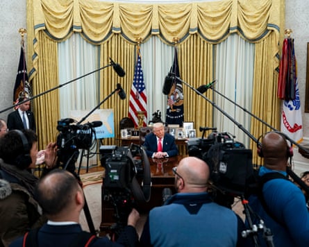 Camera operators and sound recordists with mike booms in a huddle in front of Donald Trump who is seated at his desk