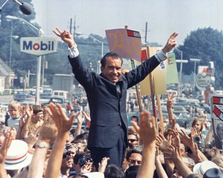 Richard Nixon standing on a platform amid a crowd, making victory signs with his hands