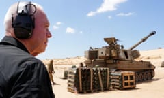 Yoav Gallant, wearing headphones, gazes at a tank and boxes of supplies near the border between Israel and Gaza.