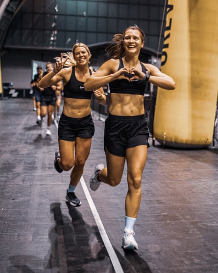 Two women run part of the Hyrox course while smiling and looking generally happy.