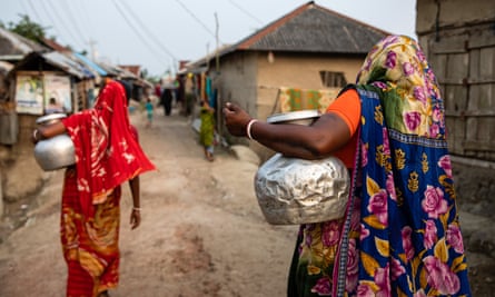Two women, seen from behind, collect drinking water in Bangladesh.