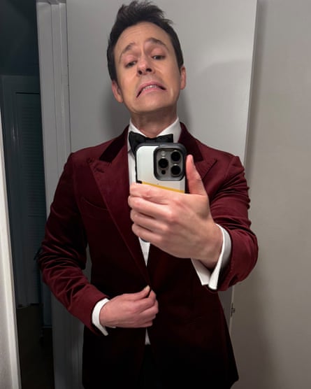 Bryan Safi in a red suit jacket, white shirt and black bow tie, taking a selfie with his phone.