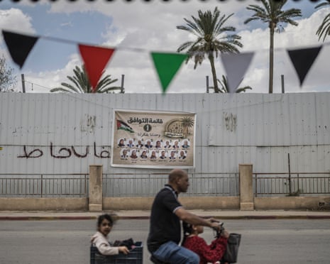 A man drives children on an electric bicycle past an election campaign banner showing candidates for the Jericho Governorate ahead of municipal elections, in the Israeli-occupied West Bank city of Jericho