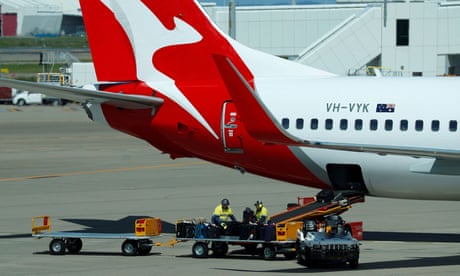 A baggage train in front of a Qantas plane on the tarmac