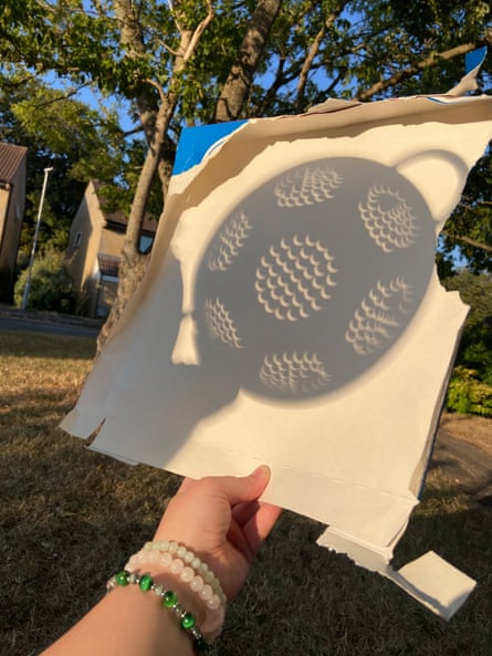 The shadow of a colander capturing the solar eclipse on a piece of cardboard
