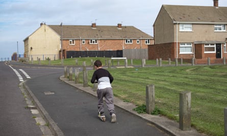 A boy rides a scooter on a footpath near houses