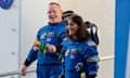 Two astronauts, one a white man and one an Indian woman, smile as, dressed in blue space suits, they walk on a ramp