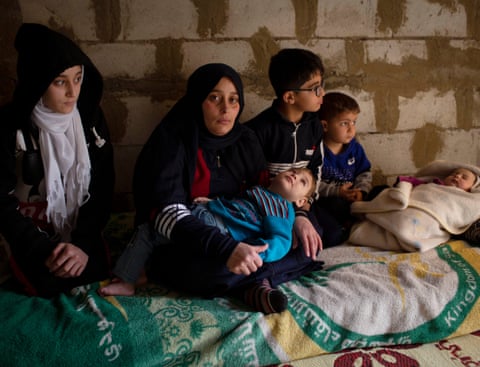 Farzad Uaz holds her two year old son, Moaz who has spina bifida, accompanied by her other four children in the unfinished apartment they are renting in Zahlé, Lebanon, 23 March 2021. 