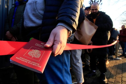 A man holds a Russian passport as he queues with others next to a red cordon