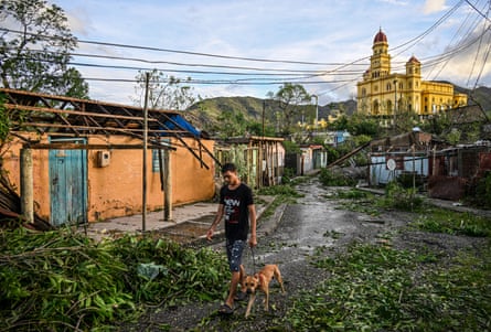 A man walks his dog past downed trees, power lines and destroyed houses in El Cobre in Santiago de Cuba, Cuba.