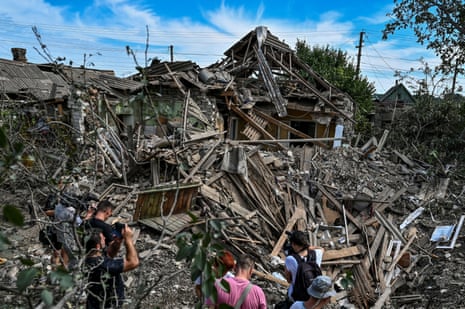 People stand next to a residential house destroyed by a Russian missile strike in the settlement of Kushuhum in Zaporizhzhia.