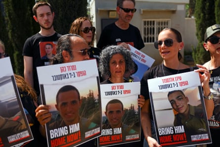 A group of people hold up placards showing pictures of hostages, all bearing the slogan BRING HIM HOME NOW