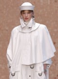 A fashion model wearing a white haute couture outfit on a catwalk with a white hat