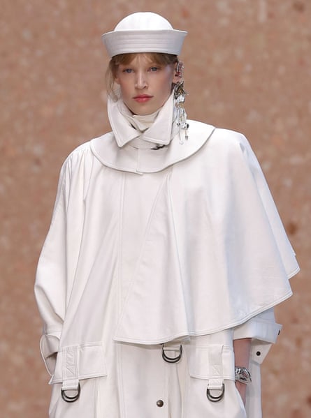 A fashion model wearing a white haute couture outfit on a catwalk with a white hat