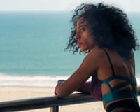 Rosalind Eleazar leans on a railing overlooking the ocean, glancing back over her shoulder