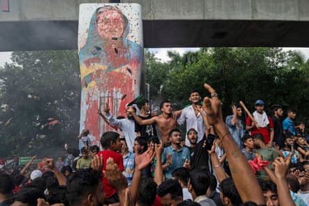 A poster covered in paint hangs from a bridge in front of a crowd of people, many with raised hands.