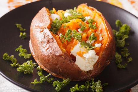 Orange sweet potatoes baked with cream cheese, spices and parsley close-up on a black plate.