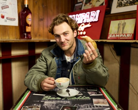Young man holds a cup of coffee and a large pastry at a table at Bar Italia in Soho.