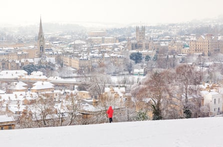 Person in a red jacket looking at the City of Bath from a snow covered hill.