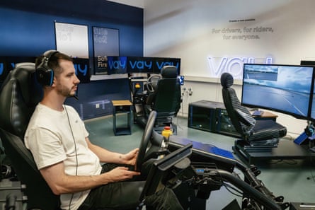 A man with headphones, holding a steering wheel while looking at screens of a road