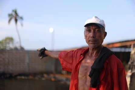 Ender Bermúdez, a fisher hired to clean crude oil from the shore, points to a nearby shrimp feed factory that pollutes the area.